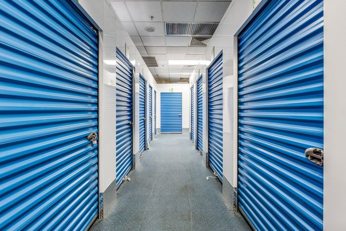 Spacious storage facility hallway with modern blue roll-up doors and bright lighting.