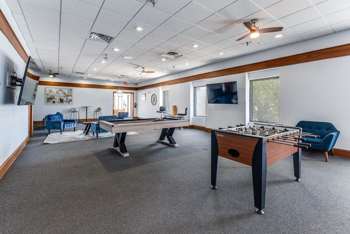 Spacious and inviting entertainment room featuring a stylish foosball table, modern pool table, and cozy seating area in a well-lit space.