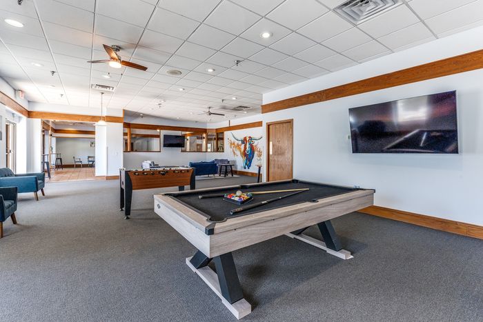 Vibrant recreational room featuring a sleek billiards table, foosball setup, cozy seating area, and modern decor with a wall mural.