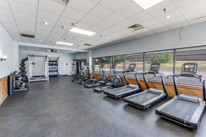 Spacious and modern fitness center featuring state-of-the-art gym equipment, including treadmills, exercise bikes, and weight machines, with a wall of windows for natural light and an inspiring view.