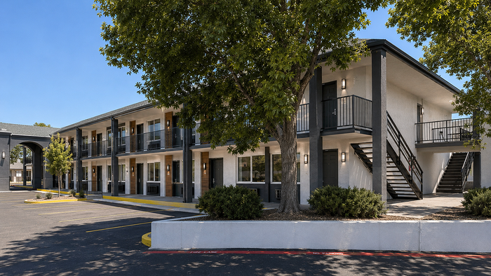 Charming two-story apartment complex with modern exterior and lush trees, featuring convenient stair access and ample parking space.