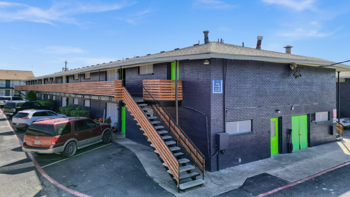 Charming apartment building with vibrant green accents and convenient parking, featuring modern wood railing and exterior stairs.