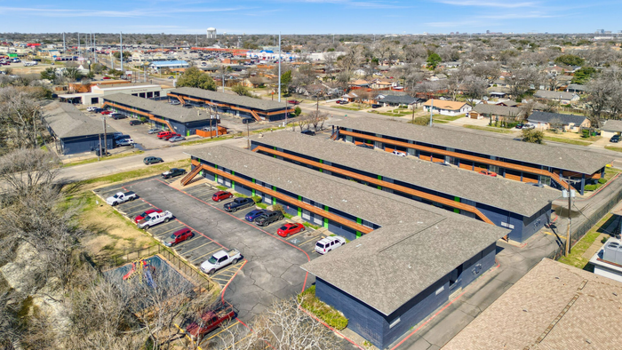 Aerial view of modern apartment complex with ample parking and vibrant community setting.