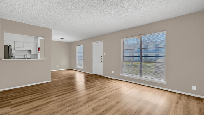 Bright and airy living space with sleek hardwood floors and large windows, seamlessly flowing into a modern kitchen.
