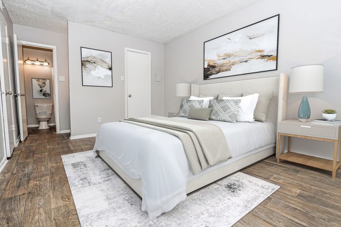 Furnished bedroom with a bedside lamp and wood-tone flooring in a Dakota Apartments unit