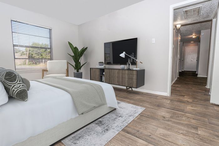 Furnished bedroom with large windows and wood-tone flooring in a Dakota Apartments unit