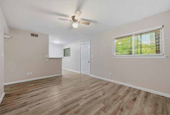 Bright and airy living space featuring sleek hardwood floors, modern ceiling fan, and ample natural light through large windows.