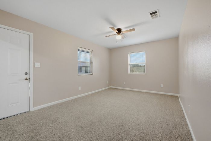 Bright and spacious bedroom with plush carpeting, two sunny windows, and a modern ceiling fan.