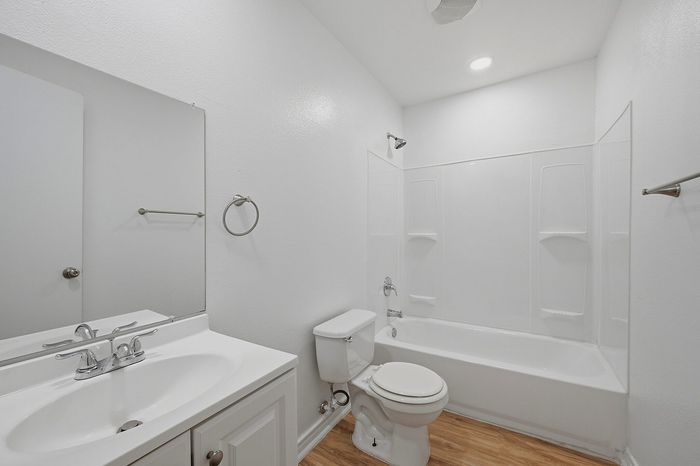 Bright, modern bathroom with sleek white fixtures, a spacious tub, and elegant wood flooring.