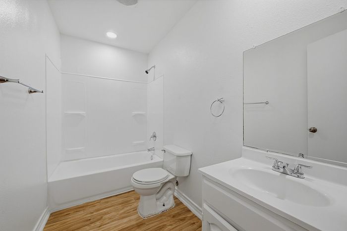 Bright and modern bathroom with sleek white fixtures, gleaming vanity, and elegant wood flooring.