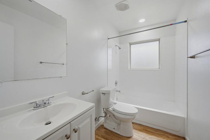 Bright and modern bathroom featuring sleek white fixtures, a spacious bathtub, and a large window for natural light.