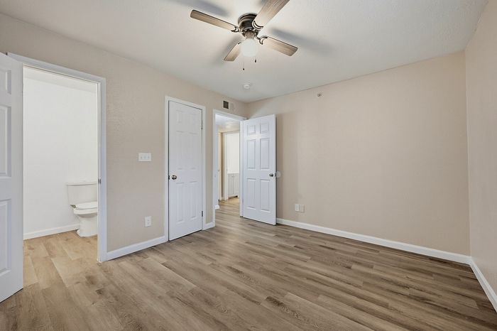 Bright and inviting empty room with elegant wood laminate flooring, neutral walls, and ceiling fan, offering a versatile space ready for personalization.