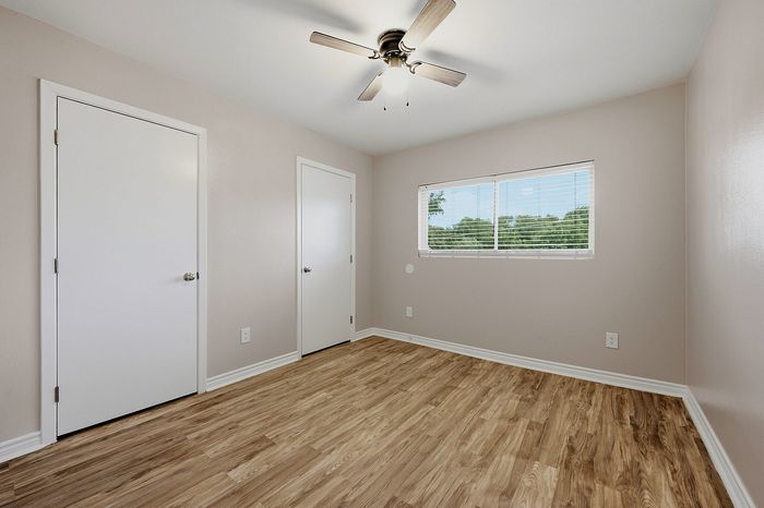 Bright bedroom with sleek laminate flooring, neutral walls, and a ceiling fan creating a welcoming, airy space.