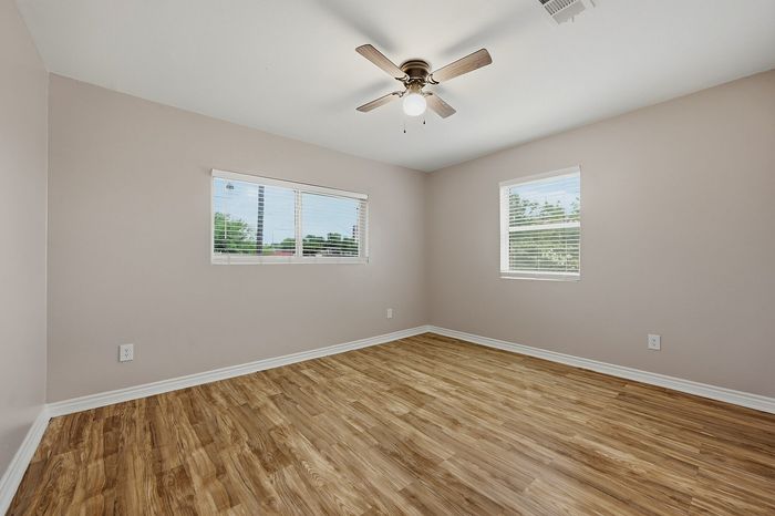 Bright and inviting bedroom with elegant wood flooring, modern ceiling fan, and ample natural light from large windows.