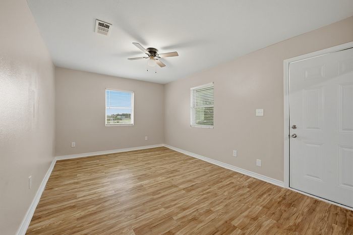 Bright, inviting room with natural light streaming through large windows, elegant wood flooring, and a sleek ceiling fan, perfect for a cozy retreat or home office.