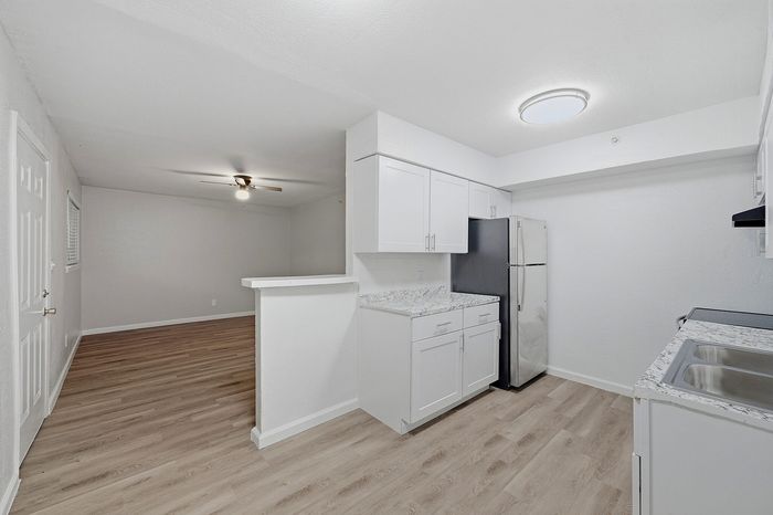 Modern apartment kitchen with sleek white cabinetry, marble countertops, and stainless steel appliances leading into a bright open-concept living area with elegant wood flooring.