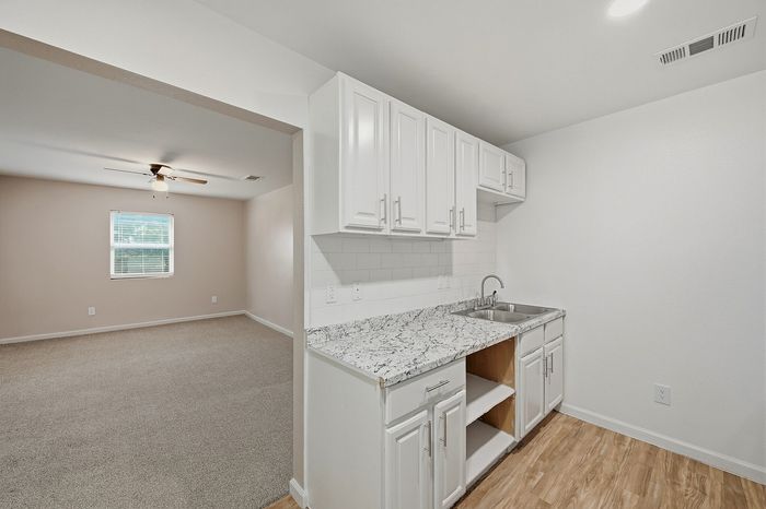 Bright and spacious kitchen with elegant white cabinets and marble countertops, leading into an inviting open living area with soft carpeting and natural light.