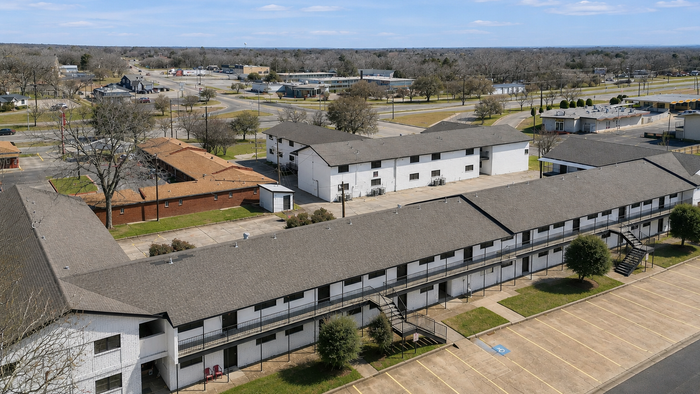 Aerial view of a spacious apartment complex with neatly arranged buildings and ample parking space in a serene suburban setting.