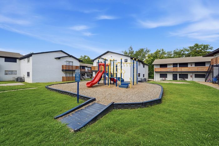 Inviting apartment complex with a vibrant playground featuring a red slide, nestled within lush green lawns, ideal for family living.