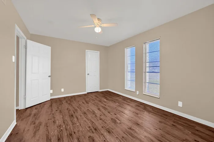 Inviting room with elegant wood flooring, modern ceiling fan, and ample natural light streaming through large windows.