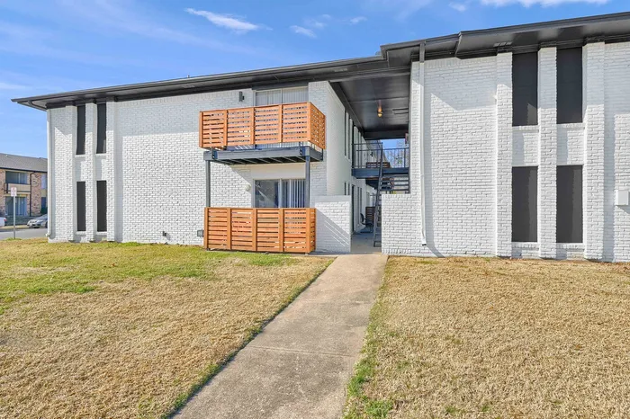 Charming white brick apartment building with modern wooden balconies and a welcoming front path.