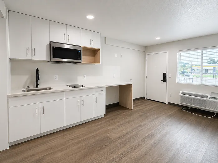 Modern apartment kitchen with sleek white cabinets, stainless steel microwave, and elegant wood laminate flooring, offering a bright and functional space.