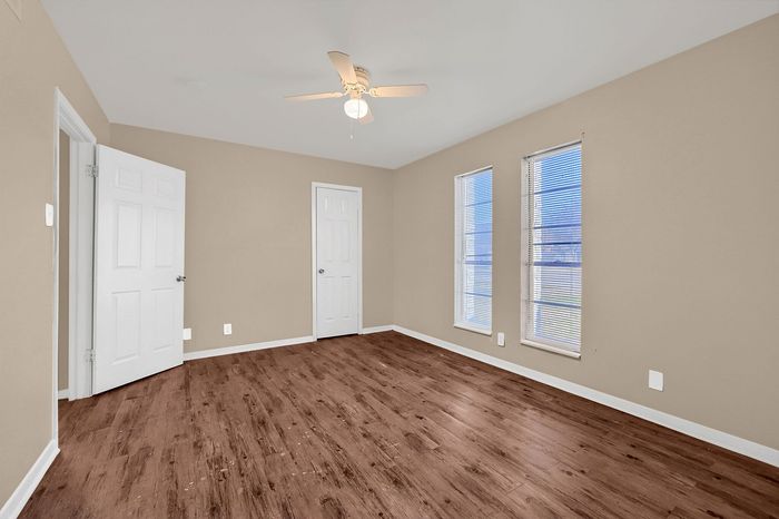 Bright and airy room featuring elegant wooden flooring and large windows with a ceiling fan, perfect for customizable living space.