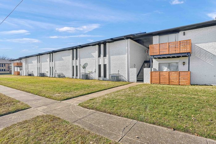 Contemporary apartment building with charming wooden balconies and crisp white brick exterior, set against a vibrant green lawn and clear blue sky.
