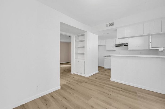 Modern apartment interior with open-concept kitchen, sleek white cabinetry, and elegant hardwood floors.