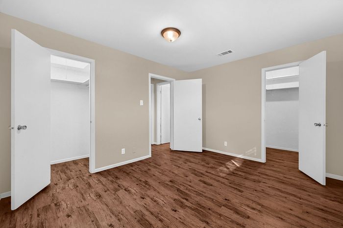 Spacious bedroom with warm wooden flooring and ample natural light, featuring multiple open doors leading to closets and other rooms.