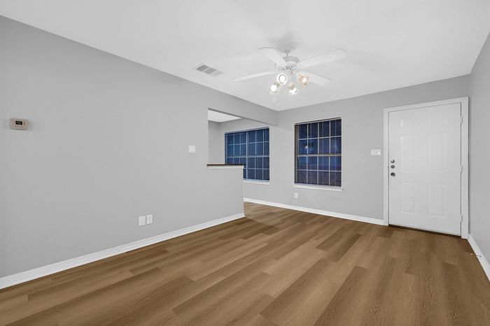 Inviting room with elegant wood flooring, modern ceiling fan, and abundant natural light from large windows.