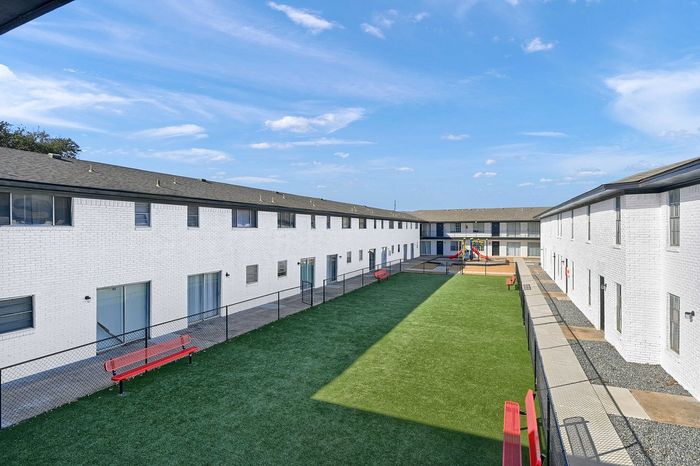 Bright and inviting apartment courtyard featuring lush green lawn, play area with vibrant playground, and sleek modern architecture.