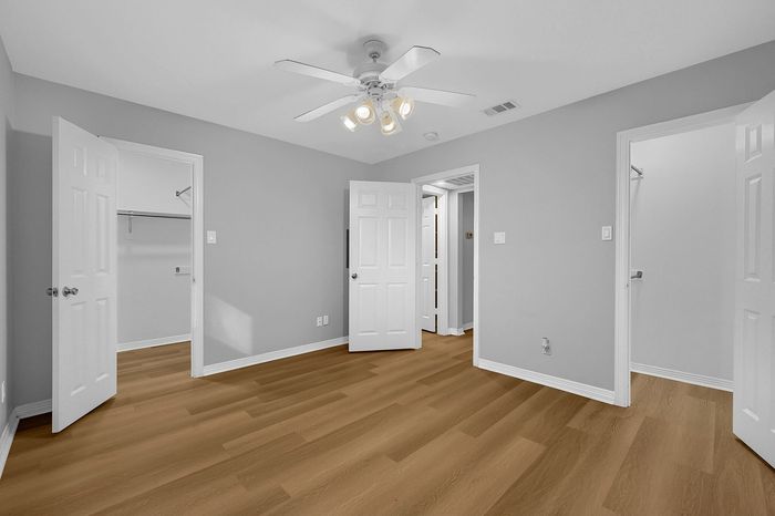 Bright room with elegant wood flooring, modern ceiling fan, and dual walk-in closets, showcasing spacious living potential.