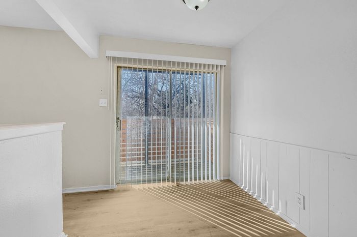 Bright apartment interior featuring sliding glass door with vertical blinds, opening to a scenic outdoor view.