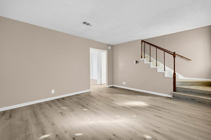 Inviting open living space with beautiful wood floors and elegant staircase, offering a warm and spacious atmosphere.