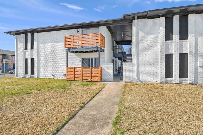 Charming apartment building with modern white brick exterior and stylish wooden balconies, nestled in a serene neighborhood with lush green lawns.