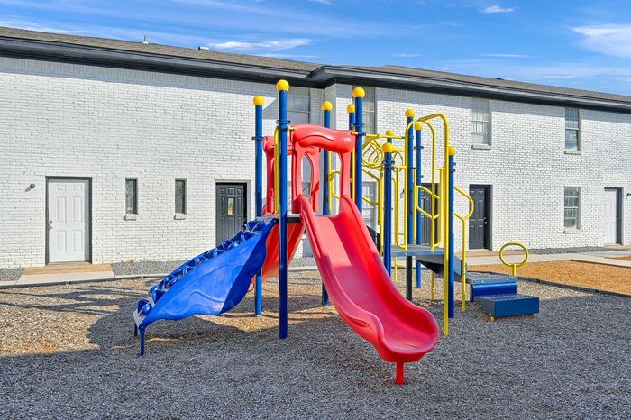 Vibrant community playground with colorful slides and climbing structures, set against a modern townhouse backdrop, perfect for family-friendly living.