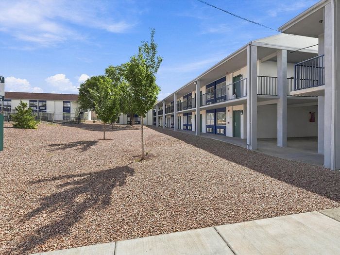 Two-story residential building with exterior walkways and courtyard trees at Juniper Flats apartments