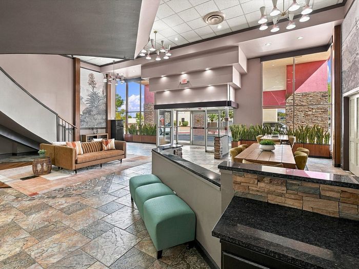 Lobby entry with glass doors, teal benches and stone-accent counter at Juniper Flats in Albuquerque, NM