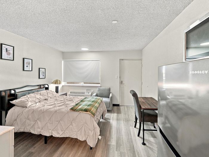 Studio apartment with bed, desk, window and wall heating and cooling unit at Juniper Flats
