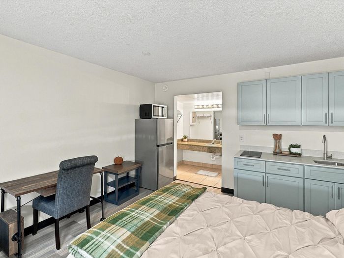 Studio apartment with gray kitchenette cabinets, sink, refrigerator and desk at Juniper Flats