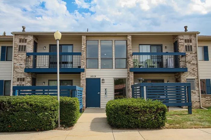 Charming two-story apartment complex with modern blue accents, private balconies, and lush landscaping.