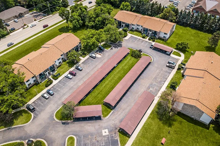 Aerial view of charming apartment complex with lush green lawns, ample parking, and inviting red-roofed buildings.
