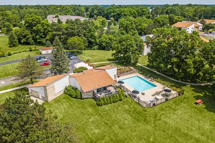 Charming aerial view of a serene apartment community featuring a sparkling pool, lush green landscapes, and inviting outdoor spaces.