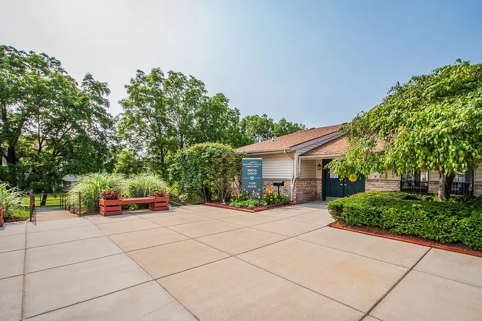Inviting rental office entrance surrounded by lush greenery and vibrant flowers, offering a warm welcome to a serene living environment.