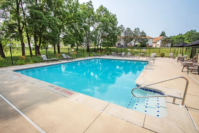 Inviting outdoor pool area with sunlit water, surrounded by lush greenery and comfortable lounge chairs.