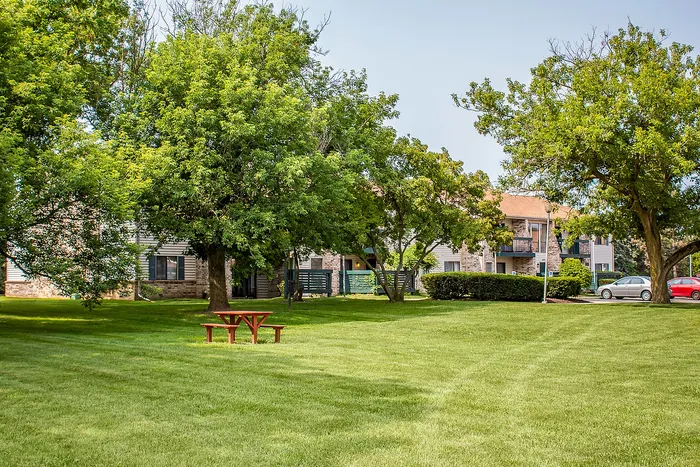 Inviting apartment complex with lush green lawns, mature trees, and a charming picnic area for outdoor relaxation.