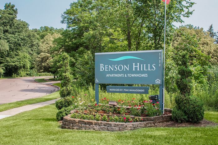 Inviting Benson Hills Apartments sign surrounded by lush greenery and vibrant flowers, offering a glimpse into a serene living environment managed by Peak Management.