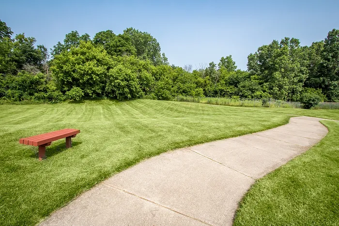 Serene park view with lush green lawns, a winding pathway, and a cozy red bench inviting relaxation.
