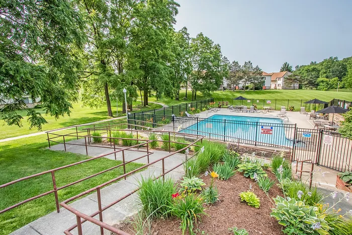 Inviting community pool area surrounded by lush greenery, featuring comfortable lounge chairs and umbrellas, ideal for relaxation and leisure.